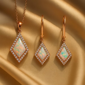 May include: A jewellery set consisting of a necklace and two drop earrings. Each piece features a kite-shaped opal stone surrounded by a halo of small clear stones, all set in a warm-toned metal. The necklace includes a delicate chain.