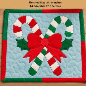 May include: A square quilted fabric piece featuring two crossed candy canes, one red and white, one green and white, tied with a large red bow and green holly leaves on a light blue background. Text reads: Finished Size : 8 * 8 Inches A4 Printable PDF Pattern.