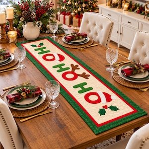 Könnte beinhalten: Ein rechteckiger, gesteppter Tischläufer mit cremefarbener Mitte und dem rot-grünen Schriftzug HO HO HO, verziert mit einer Weihnachtsmannmütze, Rentiergeweih und Stechpalmenblättern. Der Läufer hat einen breiten grünen Rand mit Muster.