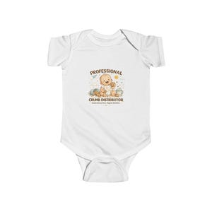 May include: A white short-sleeve baby bodysuit featuring a graphic of a smiling baby holding a cookie. The text reads PROFESSIONAL CRUMB DISTRIBUTOR and Snacks Everywhere, Regrets Nowhere, surrounded by small illustrations of crumbs and a cup.