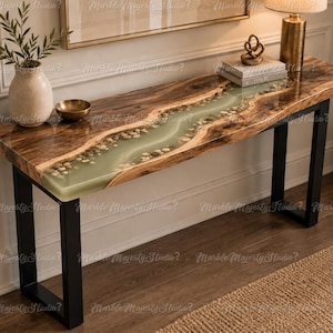 May include: A rectangular console table featuring a live edge wood slab with a central river-like inlay of translucent light green resin embedded with small smooth river stones, supported by two black metal U-shaped legs on a wooden floor.