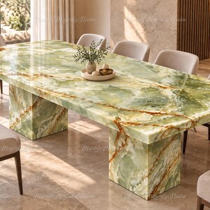 Puede incluir: Una mesa de comedor rectangular con una superficie de piedra ónix verde pulida con vetas marrones prominentes y dos bases de pedestal tipo bloque a juego, rodeada por ocho sillas tapizadas con tela beige claro y patas de madera oscura.