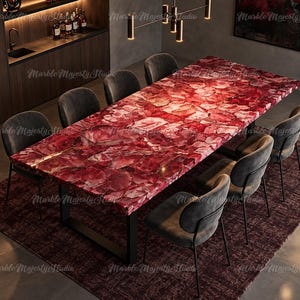 Op de afbeelding: Een rechthoekige eettafel met een gepolijst oppervlak van rode edelsteen, bestaande uit een mozaïek van onregelmatige karmozijnrode en bordeauxrode steenfragmenten. De tafel rust op een zwart metalen frame en is omringd door acht donkergrijze gestoffeerde stoelen.