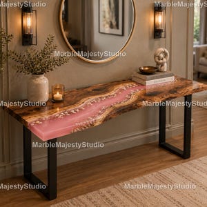 May include: A rectangular console table featuring a natural wood slab top with a central river-like inlay of translucent pink resin embedded with small stones. The table is supported by two black metal U-shaped legs and has a smooth finish.