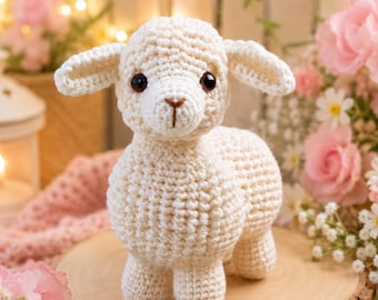 May include: A cream-colored crocheted lamb stuffed animal featuring a textured yarn body, floppy ears, and dark brown safety eyes. The lamb has a small, stitched brown nose and mouth detail, standing on four short legs with a rounded, plush appearance.