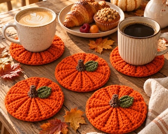 May include: A set of four round, orange, crocheted pumpkin-shaped coasters. Each coaster features a textured, ribbed design with a small brown stem and a single green leaf attached to the center. The coasters are arranged on a wooden surface.