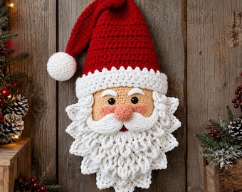 May include: A crocheted Santa Claus wall hanging featuring a red hat with a white pom-pom, a beige face with black eyes, a pink nose, and a thick white beard made of textured yarn loops. The ornament is suspended by a thin string.