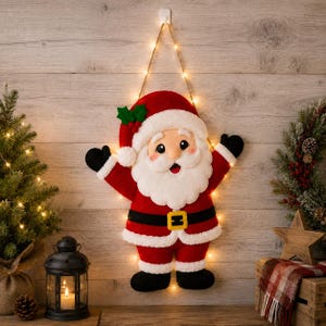 May include: A plush Santa Claus wall hanging featuring a red suit with white faux fur trim, a black belt with a yellow buckle, and black boots. The figure has a white beard, a red hat with green holly leaves, and is illuminated by string lights.