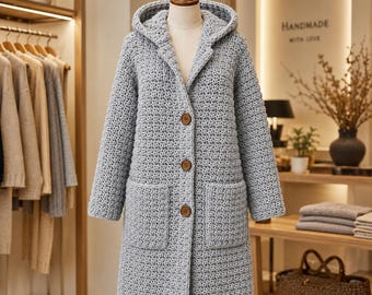 May include: A light gray hooded cardigan made of thick, textured crochet yarn. This long-sleeved garment features a hood, three large brown buttons down the center front, and two square patch pockets on the lower front section of the coat.