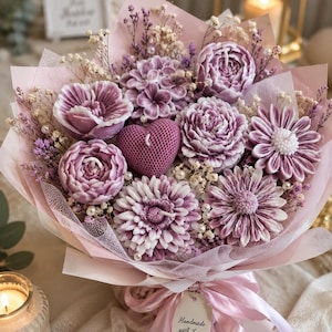 May include: A bouquet of purple flower-shaped candles and a central heart-shaped candle, accented with dried flowers and white pearls. The arrangement is wrapped in light pink paper and tied with a pink ribbon featuring a tag that reads Handmade with Love.