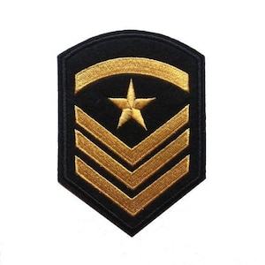 May include: A shield-shaped embroidered patch featuring a black background with gold-colored thread detailing. The design includes a curved gold bar at the top, a single five-pointed gold star in the center, and three gold chevrons below the star.
