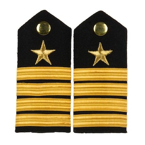 May include: A pair of black shoulder boards featuring four horizontal gold stripes and a single embroidered gold star centered above the stripes. Each board is topped with a polished gold-tone metal button at the pointed end of the fabric.