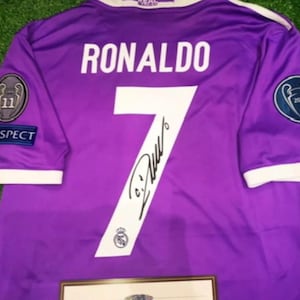 May include: A purple short-sleeved sports jersey featuring the name RONALDO and the number 7 in white on the back. The jersey includes a black signature across the number, a Respect patch, and two circular Champions League patches on the sleeves.
