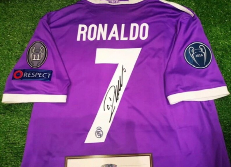 May include: A purple short-sleeved sports jersey featuring the name RONALDO and the number 7 in white on the back. The jersey includes a black signature across the number, a Respect patch, and two circular Champions League patches on the sleeves.