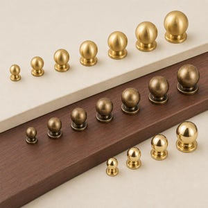 May include: A collection of spherical cabinet knobs arranged in three rows by finish and size. The top row features matte gold, the middle row displays antique bronze, and the bottom row shows polished gold, each with a circular base and stem.