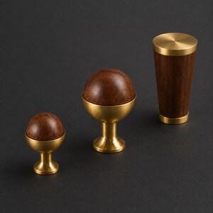 May include: Three cabinet knobs and pulls made of dark brown wood and brushed brass. Two knobs feature a spherical wooden top set on a brass pedestal base, while the third is a cylindrical pull with brass caps at the top and bottom.