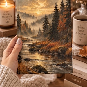 May include: A rectangular hardback book featuring a landscape illustration of a river flowing through a forest at sunset. The scene depicts tall pine trees, misty mountains, and golden light reflecting on the water. The cover art uses warm orange, brown, and green tones to portray a serene natural environment.