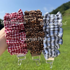 May include: Three fabric wristlet keychains with ruffled designs. The left one features a red and white gingham pattern, the center one has a brown and black cheetah print, and the right one displays a black and white striped pattern.