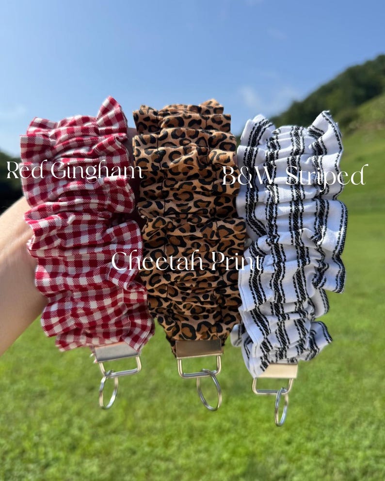 May include: Three fabric wristlet keychains with ruffled designs. The left one features a red and white gingham pattern, the center one has a brown and black cheetah print, and the right one displays a black and white striped pattern.