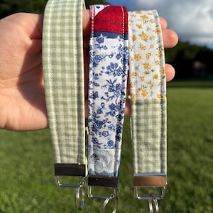 May include: Three fabric wristlet keychains with silver-tone metal hardware and split rings. The left is light green gingham, the center features a red, white, and blue floral patchwork pattern, and the right combines yellow floral and green gingham.