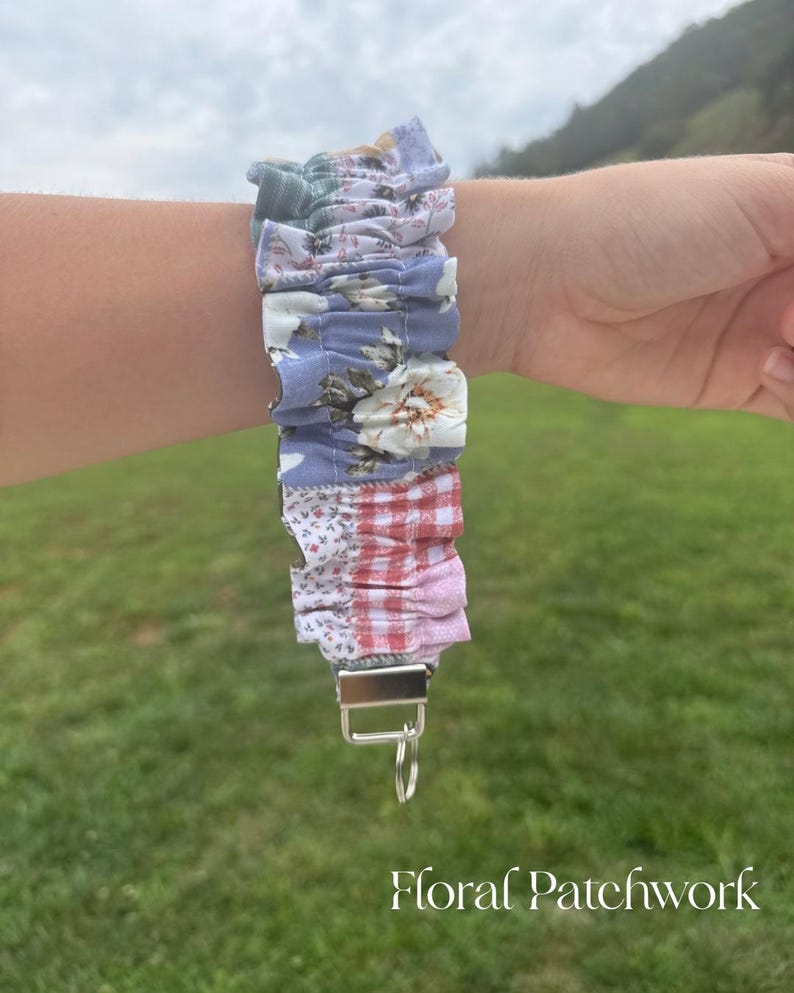 May include: A fabric wristlet keychain featuring a gathered, ruffled design with a patchwork pattern of blue, white, and red floral and gingham prints. The strap is attached to a silver-toned metal clasp with a circular split ring for keys.