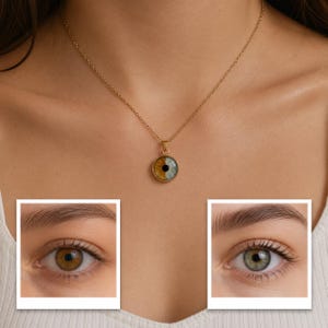 May include: A gold-toned necklace featuring a circular pendant with a split-colour iris design. One half of the iris is brown and the other half is green, centred with a black pupil. The pendant hangs from a delicate gold-toned chain.
