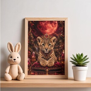 Könnte beinhalten: Ein gerahmter rechteckiger Wandkunstdruck, der ein Leopardenjunges mit einer juwelenbesetzten Krone und einem Halsband zeigt, das auf einem roten Samtkissen ruht. Der Hintergrund zeigt eine dunkle Waldszene unter einem großen roten Mond mit Kristallen.