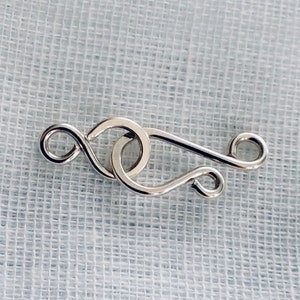 May include: Silver-toned metal clasp with a looped design. The clasp is a jewelry finding used to connect two ends of a necklace or bracelet.