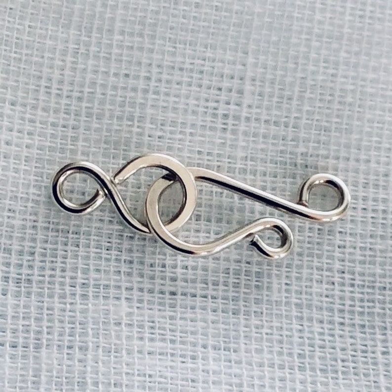 May include: Silver-toned metal clasp with a looped design. The clasp is a jewelry finding used to connect two ends of a necklace or bracelet.