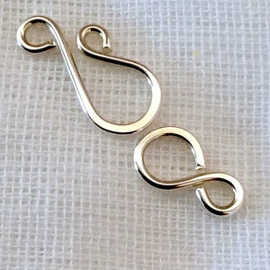 May include: Two silver metal clasps, one shaped like a figure eight and the other shaped like a teardrop with a loop at the top.