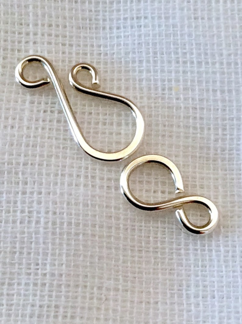 May include: Two silver metal clasps, one shaped like a figure eight and the other shaped like a teardrop with a loop at the top.