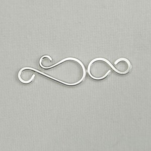 May include: Silver-toned metal clasp with a double loop design. The clasp is made of two interlocking loops, creating a secure closure for jewelry or other crafts.
