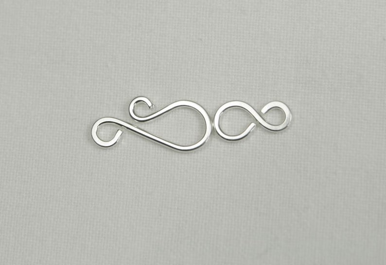 May include: Silver-toned metal clasp with a double loop design. The clasp is made of two interlocking loops, creating a secure closure for jewelry or other crafts.