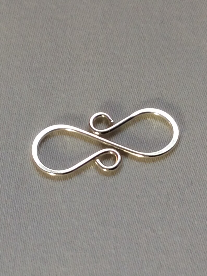 Puede incluir: Cierre de metal plateado con un dise&ntilde;o de ocho. El cierre est&aacute; hecho de un solo alambre doblado en dos bucles.