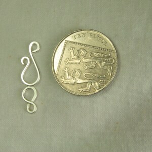 May include: Silver-toned metal jewelry clasp with two loops. The clasp is about the size of a British ten pence coin.