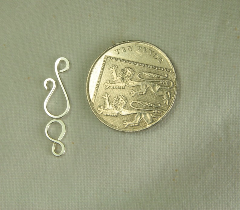 May include: Silver-toned metal jewelry clasp with two loops. The clasp is about the size of a British ten pence coin.