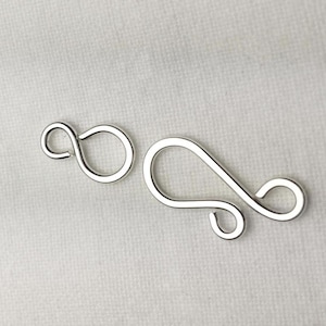 May include: Two silver-toned metal clasps for jewelry making. The clasps are in the shape of a figure eight and a sideways S.