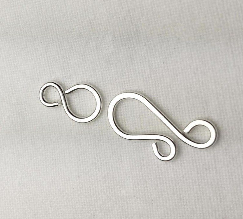 May include: Two silver-toned metal clasps for jewelry making. The clasps are in the shape of a figure eight and a sideways S.