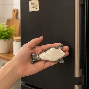 Könnte beinhalten: Ein fischförmiger Magnet mit einer glatten, cremefarbenen Mitte und strukturierten, dunkelgrauen Rändern. Der Magnet zeigt ein detailliertes Flossen- und Schwanzdesign, das mit einem Kontrastfinish die Fischform auf der Oberfläche betont.