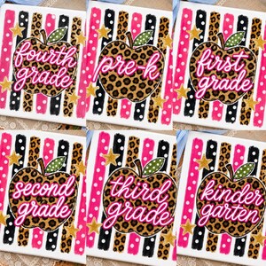 May include: Six white rectangular signs featuring vertical stripes in pink, black, and leopard print. Each sign displays a leopard print apple with a green polka dot leaf, gold stars, and pink cursive text reading fourth grade, pre-k, first grade, second grade, third grade, and kindergarten.