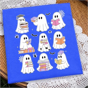 May include: A bright blue t-shirt featuring a graphic print of nine white ghosts reading various colorful books. The ghosts are surrounded by small black spiders, spiderwebs, and bats. One ghost wears a graduation cap and black glasses.