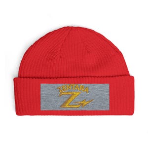 Peut inclure: Un bonnet en tricot rouge vif avec un écusson rectangulaire gris sur le revers avant. L'écusson présente le mot ZENTARA brodé en doré au-dessus d'une grande lettre Z dorée stylisée qui intègre un motif en forme d'éclair.