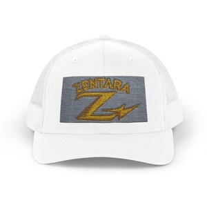 Peut inclure: Une casquette trucker blanche avec un écusson rectangulaire gris sur le devant. L'écusson affiche le mot ZENTARA brodé en doré au-dessus d'une grande lettre Z dorée stylisée qui intègre une forme d'éclair dans son design.