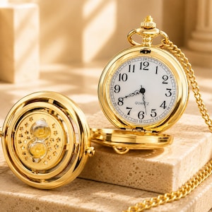 May include: A gold-tone pocket watch with a white face, black Arabic numerals, and the word QUARTZ printed on the dial. The watch features a matching gold chain and a circular cover decorated with a cutout star pattern and a central hourglass.