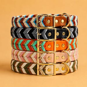 May include: A stack of five braided collars featuring gold-toned metal buckles and D-rings. Each collar displays a distinct chevron pattern in various color combinations, including brown, black, orange, pink, and olive green with white accents.