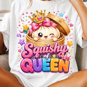 Może przedstawiać: Biały t-shirt z grafiką przedstawiającą uroczą, mrugającą postać pierożka w złotej koronie i różowej kokardzie, siedzącą w bambusowym parowniku. Napis Squishy of QUEEN wykonany jest kolorowymi, grubymi literami w otoczeniu gwiazdek.