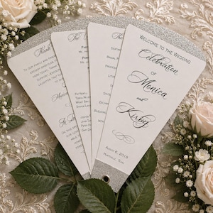May include: White wedding fan programs with silver glitter trim. The programs are fanned out, displaying text that reads "Welcome to the Wedding Celebration of Monica and Kirby" and the date August 6, 2018.