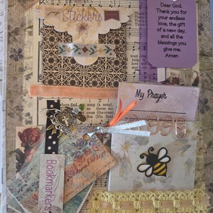 May include: A decorative scrapbook page featuring a prayer card with the text Dear God, Thank you for your endless love, the gift of a new day, and all the blessings you give me. Amen, a My Prayer card, a bee sticker, paper clips, and ribbons.