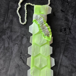 May include: A neon green necktie featuring a white braided cord neck strap, a silver metallic ruffled accent near the top, and multiple translucent white hexagonal plastic overlays attached to the front surface with small white stitches.