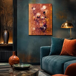 Op de afbeelding: Een rechthoekig abstract schilderij met warme koper-, oranje- en bruintinten met cirkelvormige motieven, weergegeven op een donkerblauwe muur boven een blauwe fluwelen bank met oranje kussens en een metalen vloerlamp in de kamer.